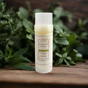 Solid lotion tube of hydrating herbal for moisturizing skin on a wood table with green leaves in background.